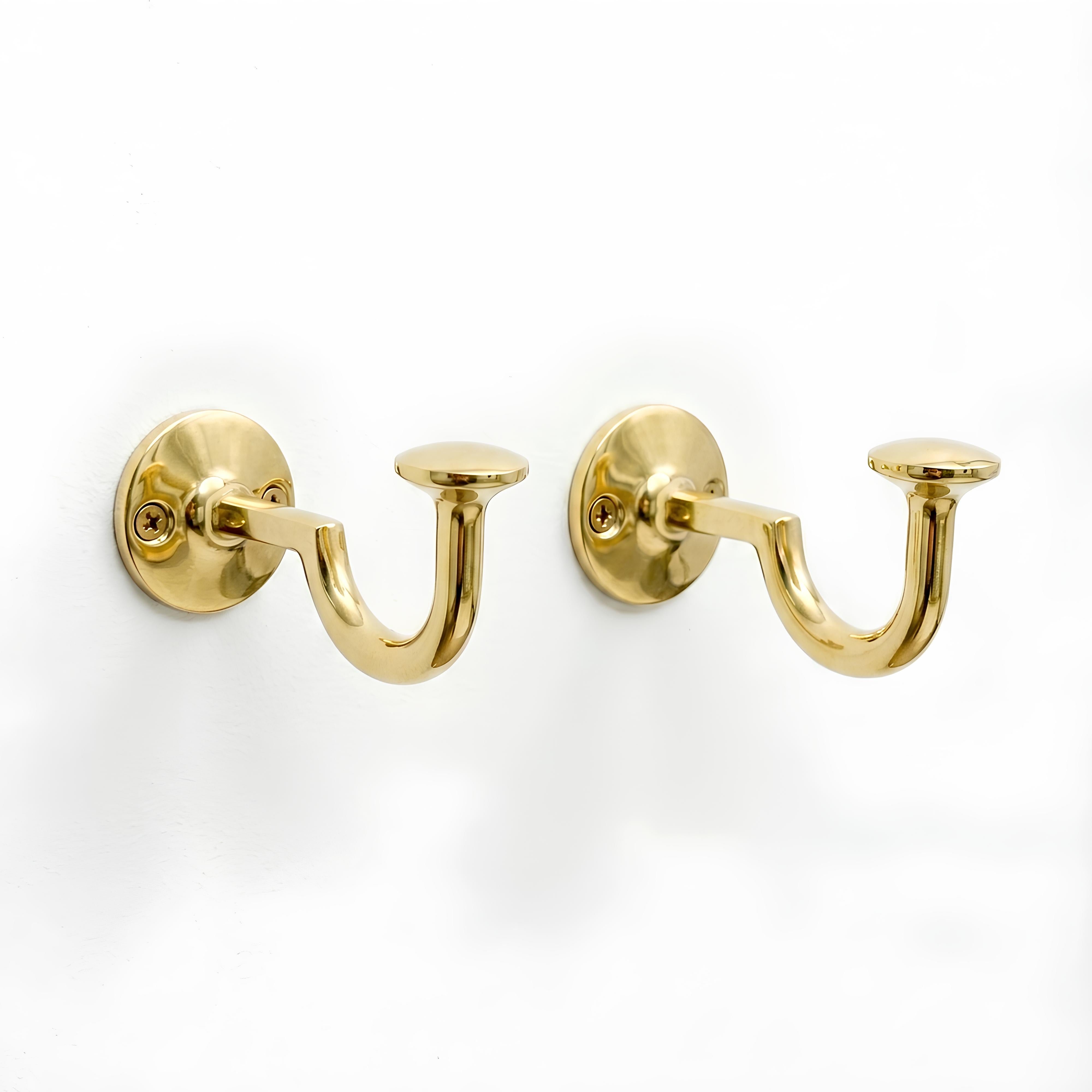 Set of two brass wall hooks with curved J-shaped design mounted on a white wall